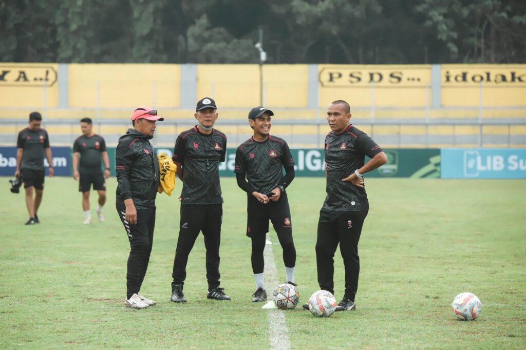 Group of Indonesian coaches discussing on the soccer field during daytime.